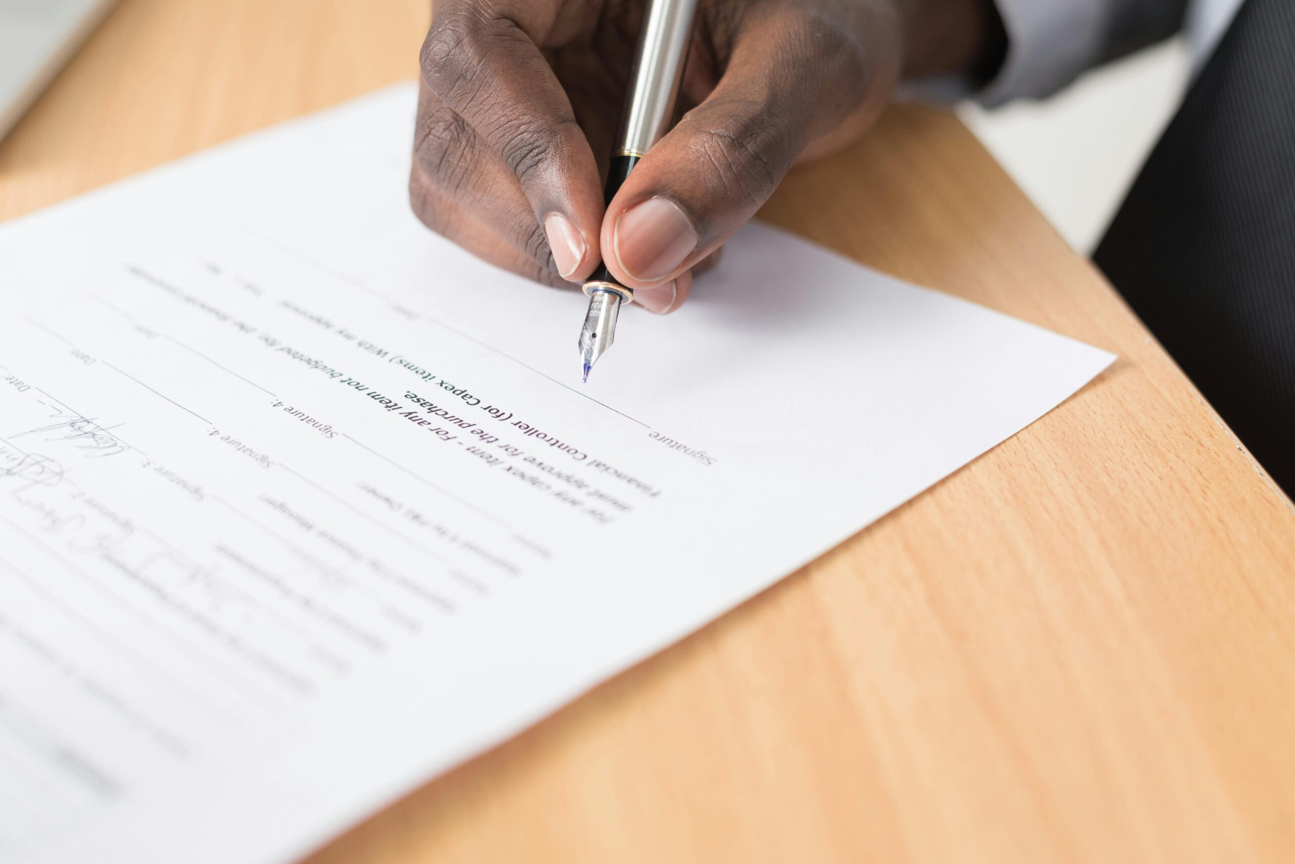 pexels-photo-955394-955394 A hand holding a pen signing a document close-up on a desk, symbolizing agreement or contract finalization.
